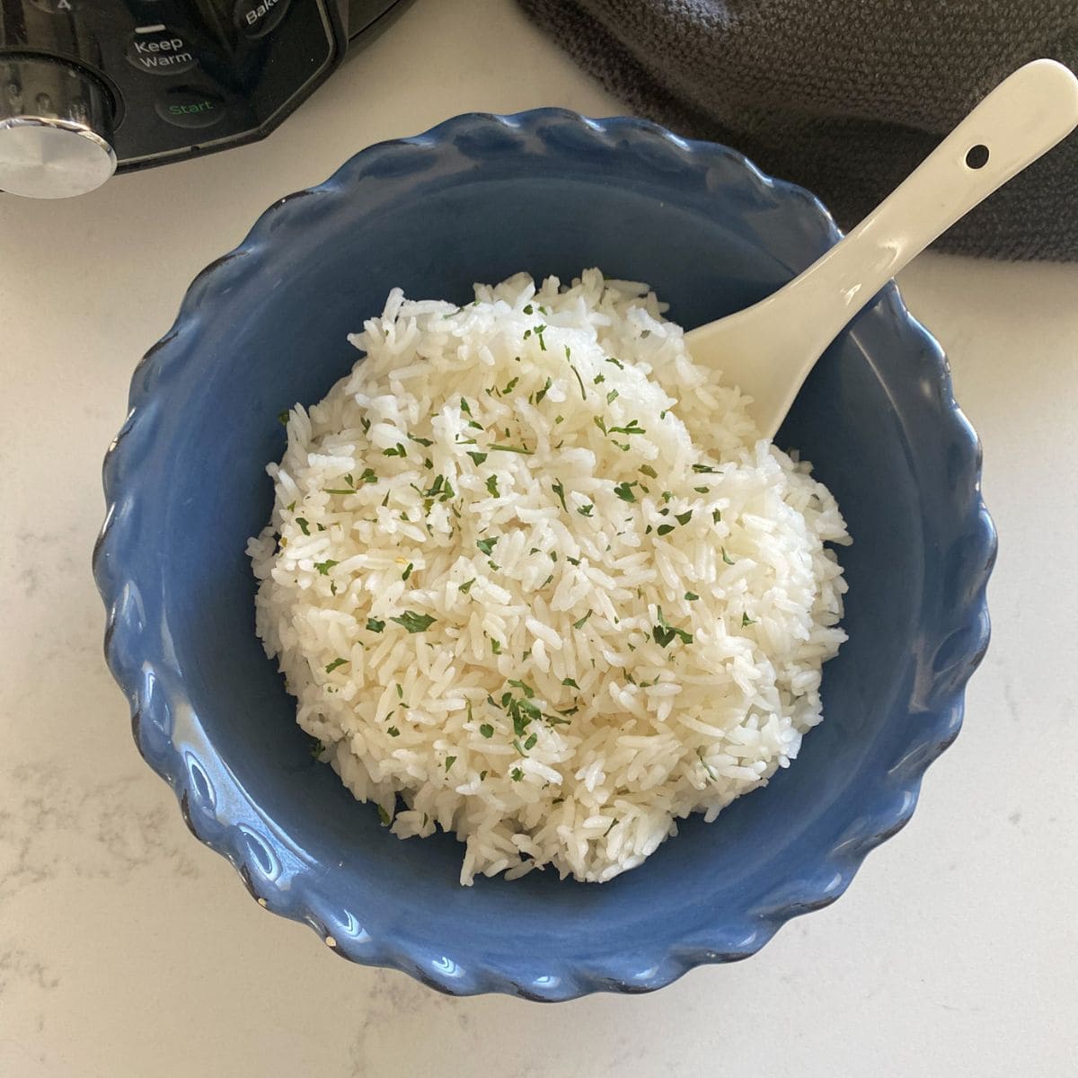 cooked jasmine rice in a blue bowl with a white spoon on a marble counter top