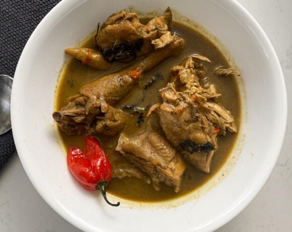 Nigerian chicken pepper soup in a white bowl with a gray towel and silver spoon to the left